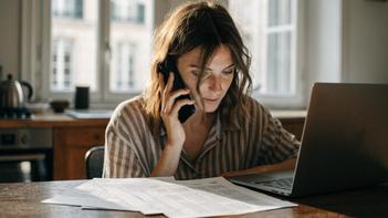 Jeune femme au téléphone à sa table de cuisine, devant un ordinateur portable et des documents, qui signale un accompagnement WIZBII insatisfaisant à son conseiller