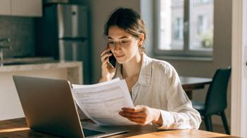 Donna seduta al tavolo di casa che legge dei moduli e parla al telefono con un consulente per capire se WIZBII è un ente ufficiale o un'azienda privata